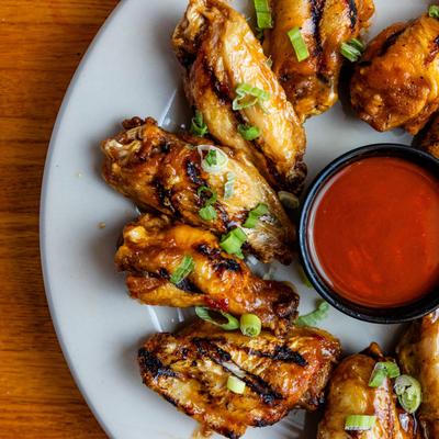 Grilled chicken wings with scallions and red dipping sauce.