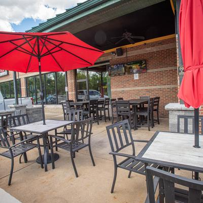 Outdoor patio featuring black metal chairs and tables shaded by red umbrellas.
