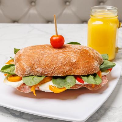 Focaccia bread sandwich with salami, mozzarella, and bell peppers, served with orange juice.