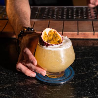 A hand placing a cocktail garnished with passion fruit  on a bar counter.