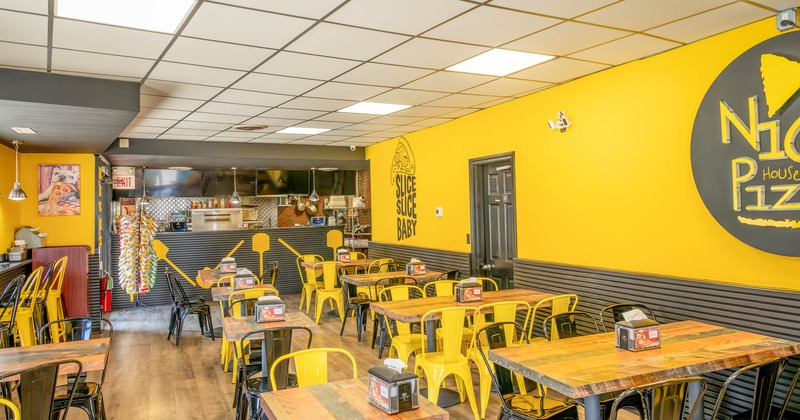 Interior of a vibrant pizzeria with yellow and black decor, wooden tables, and metal chairs
