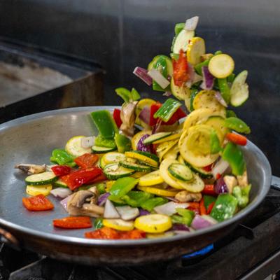 Colorful vegetables tossed in hot skillet over open kitchen flame.