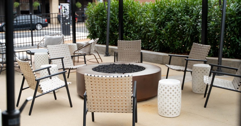 Outdoor seating area with a circular fire pit, surrounded by woven chairs and patterned stools