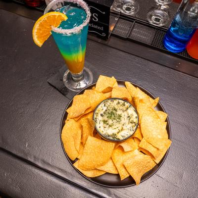 Spinach Dip with nachos served alongside a cocktail.