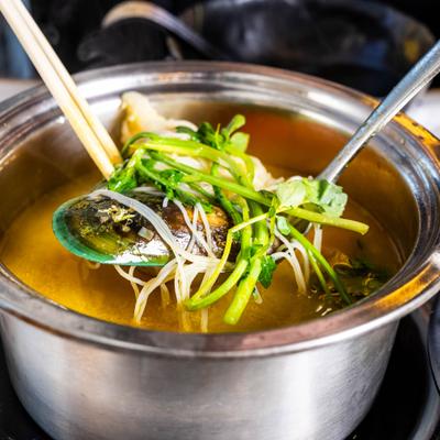 Hot pot dish featuring fresh mussels, rice noodles, and various herbs.