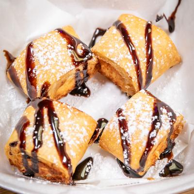 Four pastries drizzled with chocolate syrup and dusted with powdered sugar.