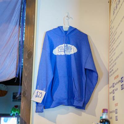 Blue hoodie with Frodo's Pizza logo hanging on a wall.