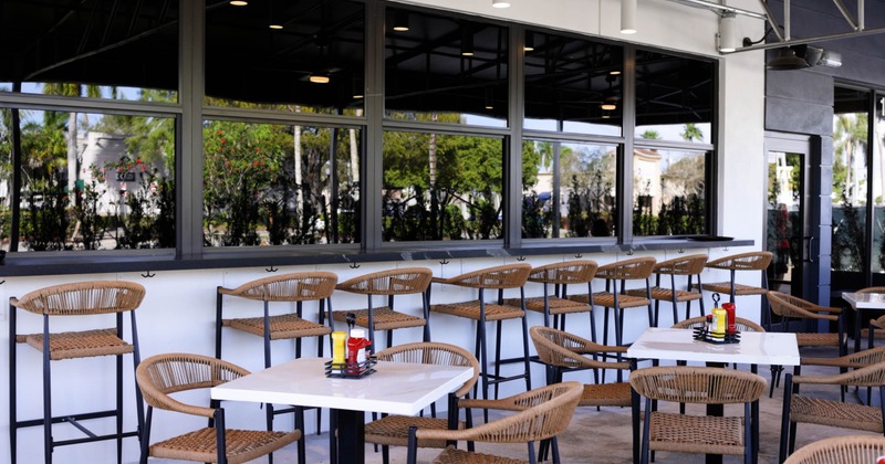 Outdoor dining area with wicker chairs and tables near large reflecting windows