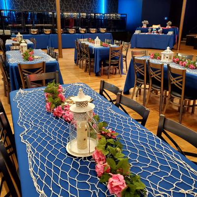 Long banquet table with a blue tablecloth, pink floral garlands, and a white lantern centerpiece.