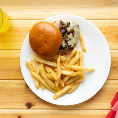 Mushroom Swiss Burger and fries, set on a light wooden table with a yellow drink.