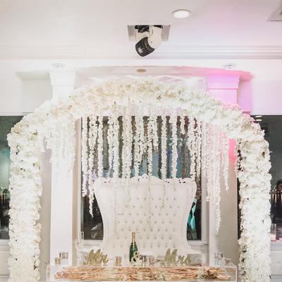 White floral arch surrounding an elegant sweetheart table.