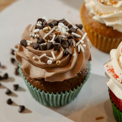 A cupcake frosted with chocolate, topped with sprinkles and chocolate chips.