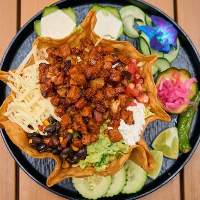 Tortilla shell filled with seasoned meat, black beans, guacamole, and shredded cheese.