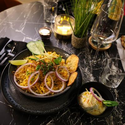Serving of biryani garnished with sliced red onions, served with sides and wine.
