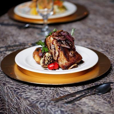 Gourmet pork chop with balsamic glaze, caramelized onions, roasted vegetables, and grilled corn.
