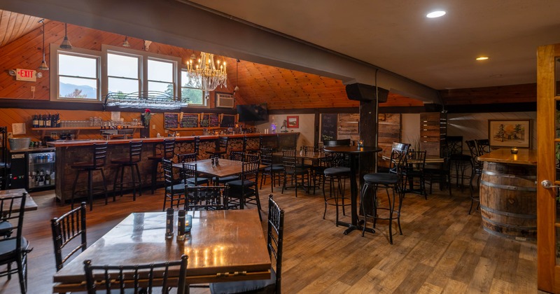 restaurant with wooden flooring, tables, and a bar area featuring shelves of bottles and a chandelier