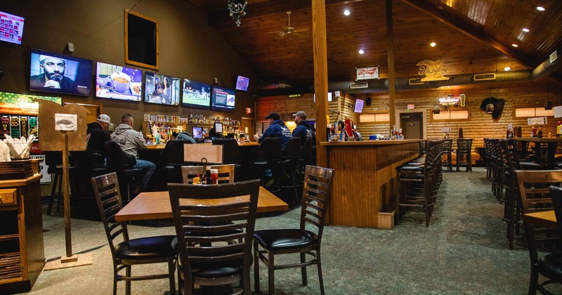 Interior, wooden tables and chairs, bar in the back, wall TV screens