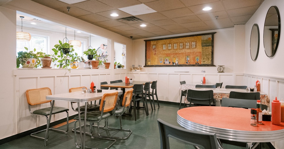 Casual dining area with tables, chairs, plants and a mural on the wall