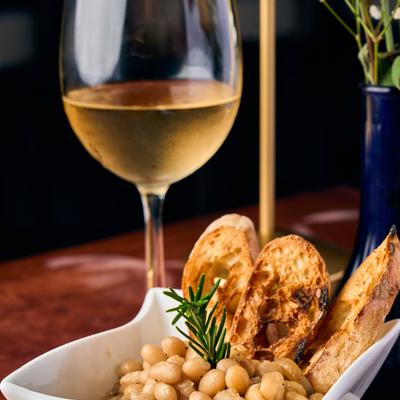 A glass of white wine served next to Tuscan white beans dish.