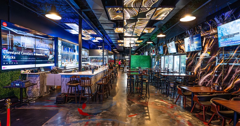 Modern sports bar and entertainment venue with a long bar and dining tables and chairs