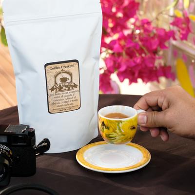 Hand holding a espresso cup beside bag of roasted beans.