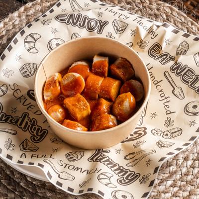 Sliced Currywurst served in a small paper bowl, dressed with a sauce.