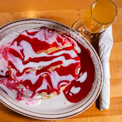 Stacked pancakes with strawberry and icing drizzle, accompanied with a mimosa cocktail.