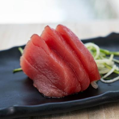 Three slices of fresh, deep red tuna sashimi resting on a platter.