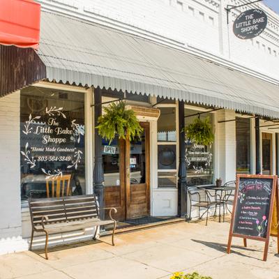 Storefront with white awning, signage, a wooden bench and a chalkboard menu.