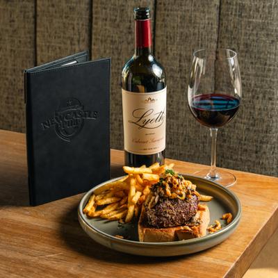 Newcastle steak with fries, alongside bottle and glass of red with and a menu.