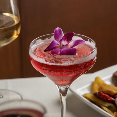 Red Eye cocktail served in a coupe glass, garnished with a purple orchid.