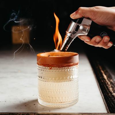 A person putting open flame to a cocktail.