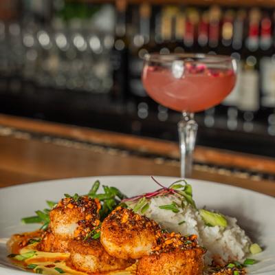 Seared scallops with rice and cocktail on a bar counter.