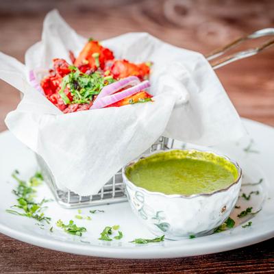 Spicy chicken with onions and herbs, accompanied by a small bowl of green dip.