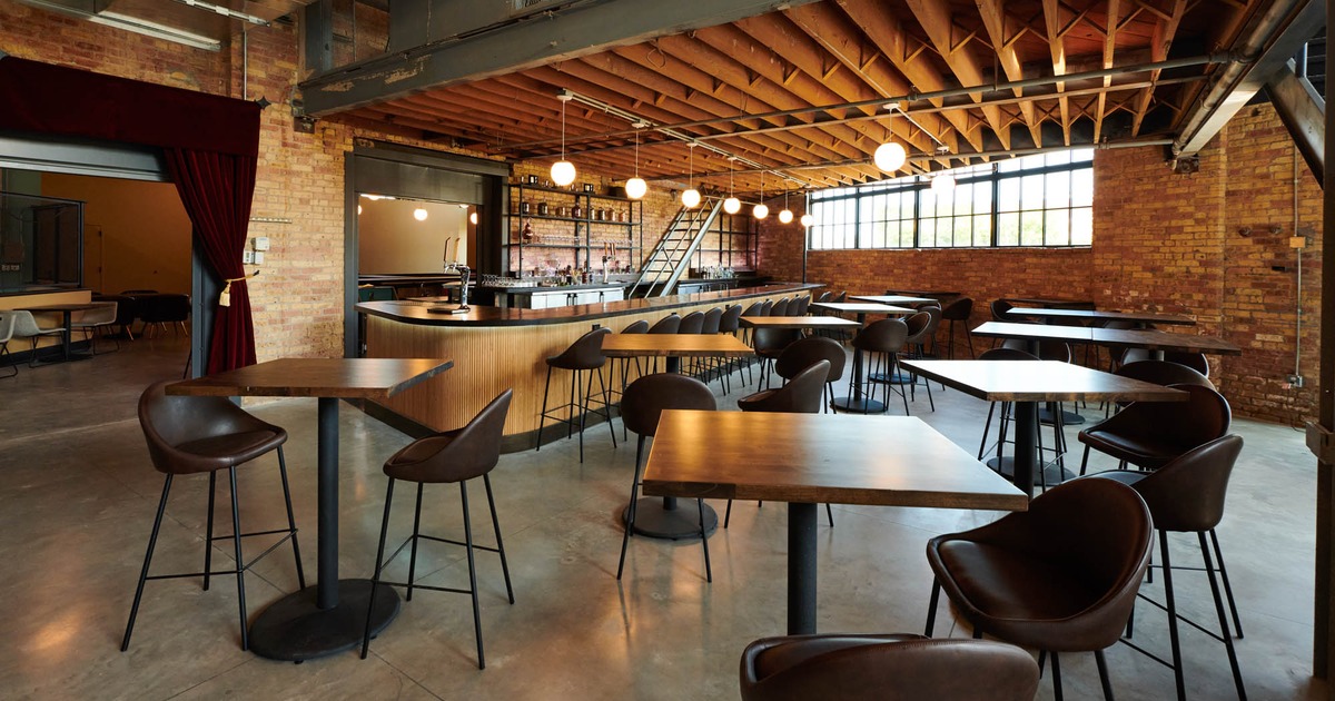 Industrial-style bar interior with wooden tables, brick walls, and pendant lighting