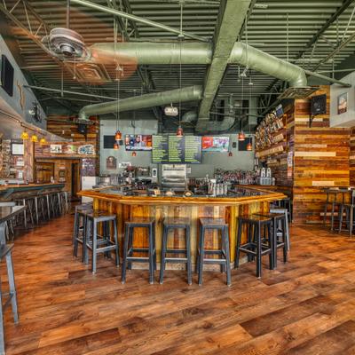 Industrial-style bar featuring a curved wooden counter with stools and exposed ceiling pipes.