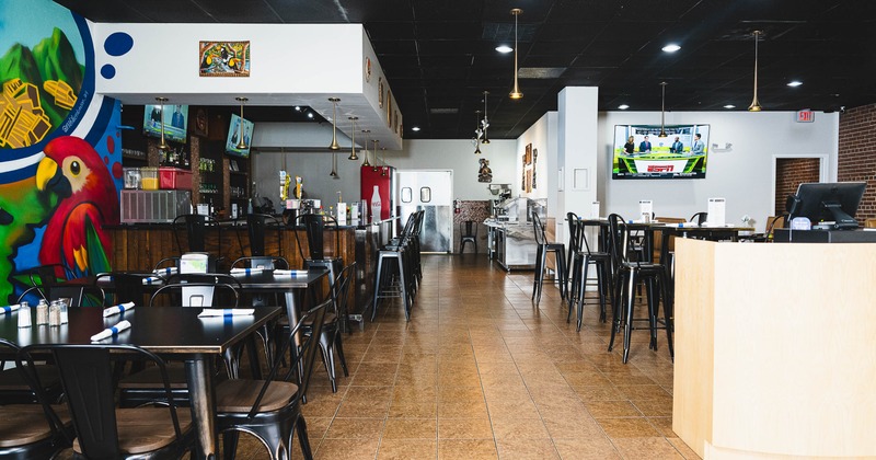 Interior of a modern restaurant with black tables and chairs, a colorful parrot mural, a wooden bar