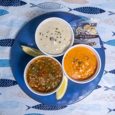 Lobster bisque, clam chowder, and seafood stew served with crackers on a blue plate.
