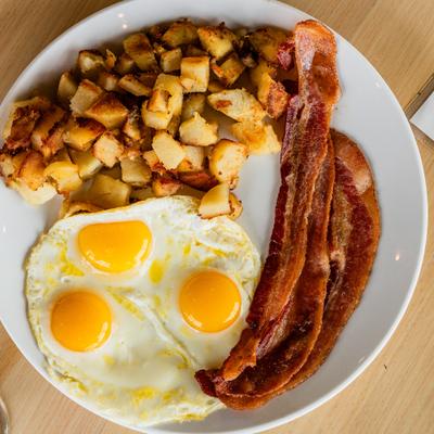 Plate with three sunny-side-up eggs, crispy bacon, and a side of home fries.