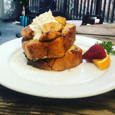 French toast with whipped cream and banana on the top, served on a patio table.