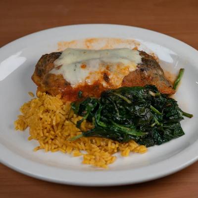 Chile relleno topped with melted cheese, served with rice and sautéed spinach.