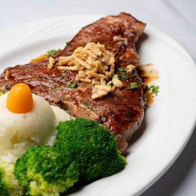 Porterhouse steak topped with fried onions, served with mashed potatoes and broccoli.