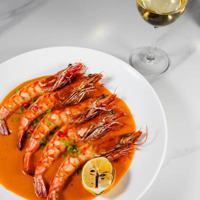 Large, head-on prawns served in a rich sauce, alongside a glass of wine.