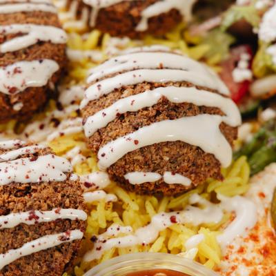 Falafel balls topped with a white sauce drizzle, served over rice, close-up.