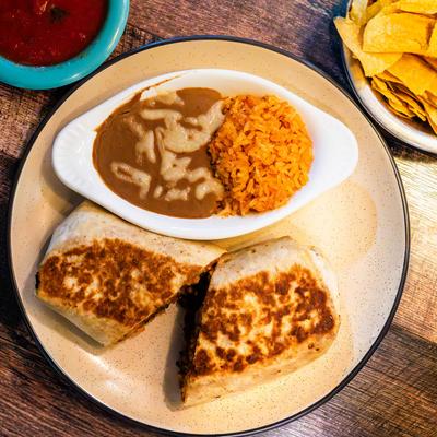 Burrito cut in half served with refried beans, rice, tortilla chips, and salsa.