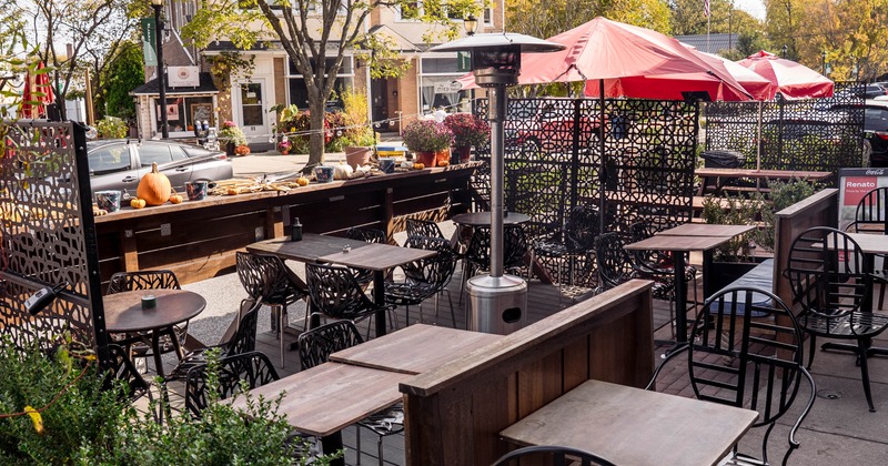 Outdoor patio with tables, red umbrellas, decorative metal screens, and autumnal decor