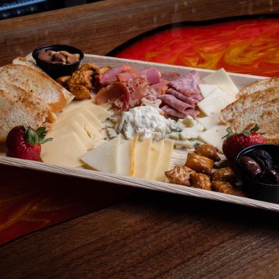 Charcuterie board with assorted cheeses, meats, bread, nuts, pretzel bites, and strawberries.