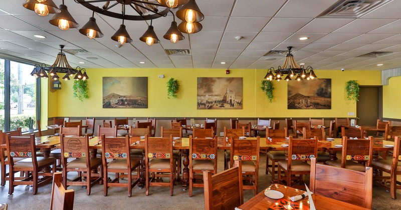 Restaurant interior with wooden furniture, yellow walls, chandeliers, paintings, and a large window