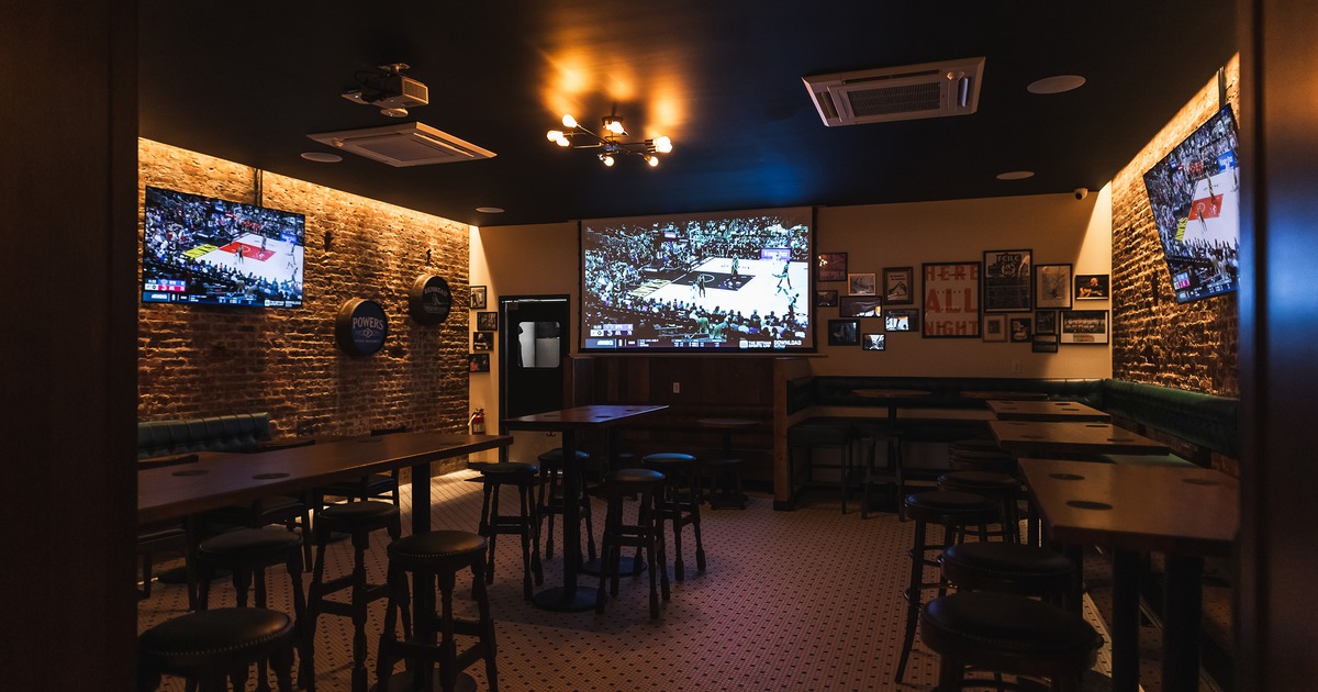 Sports bar interior with high tables, stools, booth seating along the walls, and TVs on the walls