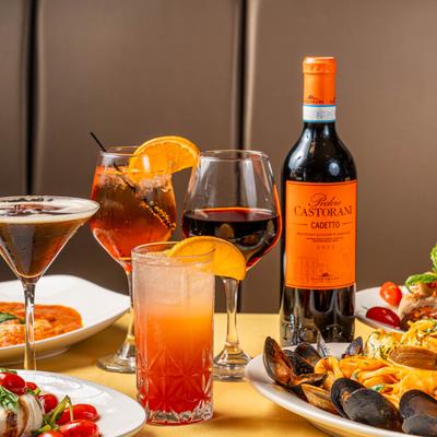 Wine and cocktails on a table with assorted food plates.